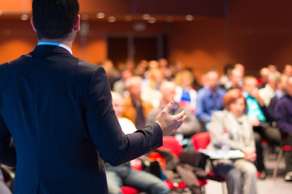 Picture of speaker presenting & audience with slightly blurred